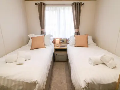 two beds in a room with a desk and a window at Curlew Lodge in Carnforth