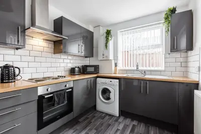 a kitchen with black cabinets and a washer and dryer at 4-Bedroom House sleeps 9 in Liverpool Perfect for Contractors - Free Parking - Fast WiFi - Fully Equipped Kitchen - Hosted by By Hinkley Homes Short Lets & Serviced Accommodation in Liverpool