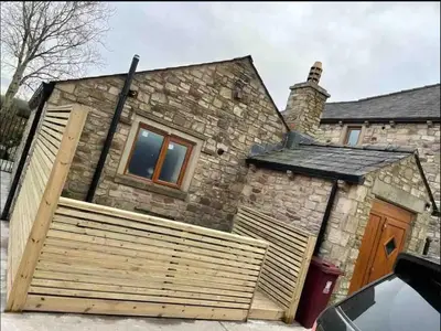 a stone house with a wooden fence in front of it at Salcombe Holiday Cottage in Wilpshire