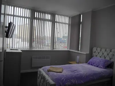 a bedroom with a bed with purple sheets and windows at Mermaid Holiday Flats in Blackpool