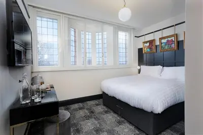 a bedroom with a bed and a table and windows at Swan & Railway Hotel Wigan in Wigan