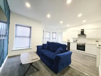 a living room with a blue couch and a kitchen at DYSA Banks Apartments in Blackpool