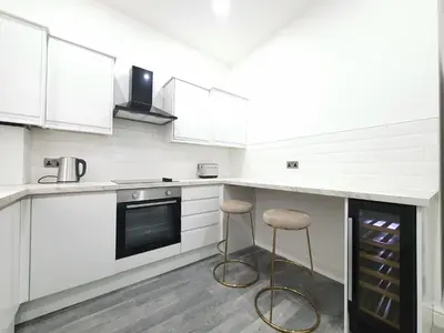 a kitchen with white cabinets and stools in it at DYSA Banks Apartments in Blackpool