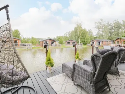 a deck with chairs and a swing and a river at Loluke Lodge on The Lake in Carnforth