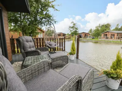 a porch with chairs and a swing and water at Loluke Lodge on The Lake in Carnforth