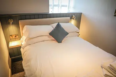 a bedroom with a white bed with a black pillow at Hope and Anchor in Flookburgh