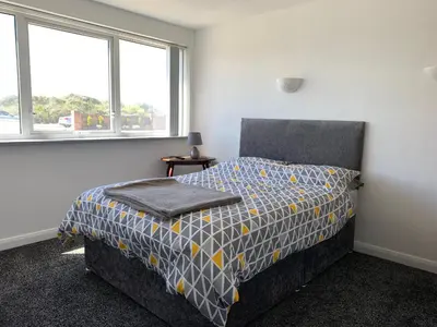 a bedroom with a bed and two windows at Beach Front Apartment with Free Parking, St Annes in Lytham St Annes