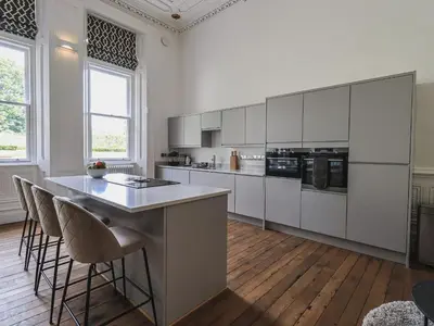 a kitchen with white cabinets and a island with bar stools at The Wilfred Suite Stone Cross Mansion in Ulverston