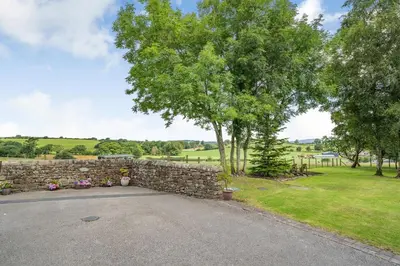 a stone wall with a tree and a driveway at Ingleborough View in Carnforth