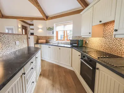 a kitchen with white cabinets and black counter tops at Oversands Cottage in Grange Over Sands