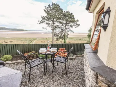 a table and chairs on a patio with a view of the ocean at Oversands Cottage in Grange Over Sands