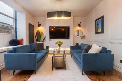 a living room with blue couches and a tv at Capri Stays - Apartment One in Blackpool