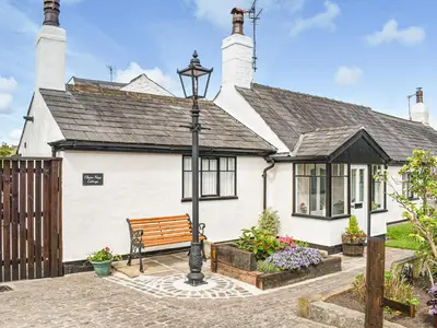 a white house with a bench in front of it at Chase Heys Cottage in Crossens