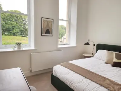 a white bedroom with a bed and two windows at The Alfred Suite Stone Cross Mansion in Ulverston