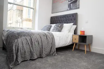 a bedroom with a bed with a gray blanket and a window at Hotel Rafay in Blackburn