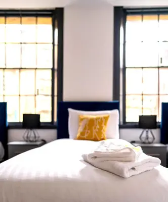 a bed with two towels on it with two windows at The Cavern Quarter Aparthotel by UStay in Liverpool