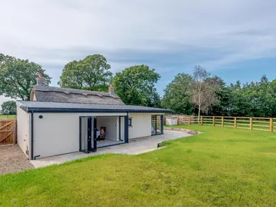 an external view of a small white building in a field at The Restored Cottage in Eccleston