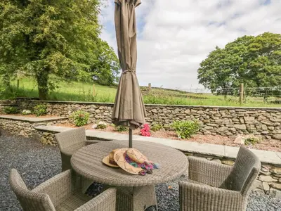a patio table with an umbrella and chairs at Bank Hurst Coach House in Ulverston