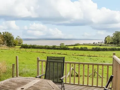 a chair on a deck with a view of the water at Little Barn in Grange Over Sands