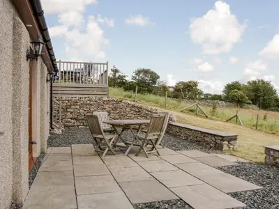 a patio with a table and chairs and a stone wall at Little Barn in Grange Over Sands