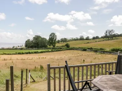 a wooden deck with a table and a view of a field at Little Barn in Grange Over Sands
