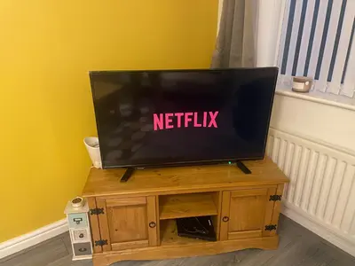 a television on a wooden stand with a netflix sign on it at warm modern 3 bedroom house free secure off road parking, wifi & sky sleep upto 6 guest 2 bathrooms in Aintree