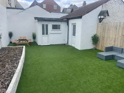 a small yard with a white house and green grass at Pleasure Beach View in Blackpool