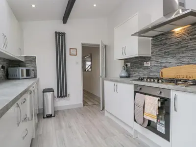 a kitchen with white cabinets and a brick wall at Harbour Retreat in Millom