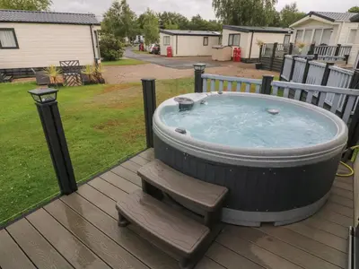 a hot tub sitting on a deck with a bench at Waterside Lodge in Carnforth