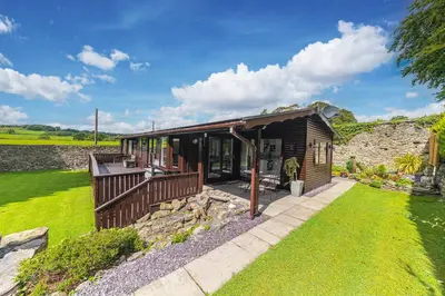 a wooden cabin with a porch and a stone wall at North Lodge Cartmel in Cartmel