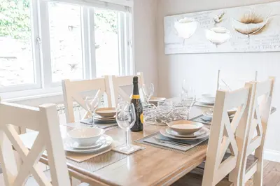 a dining room table with a bottle of wine and chairs at North Lodge Cartmel in Cartmel