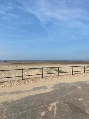 a fence on a beach with people in the background at Crosby Apartments in Liverpool