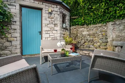 a patio with chairs and a table with a blue door at Clare's Cottage Near Cartmel - Dog Friendly, Homely, Aga, Log Burners, Disney Plus & Netflix in Holker
