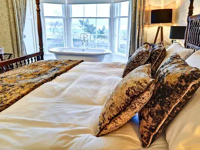a bedroom with a large bed with pillows and a tub at Bay Villa in Grange Over Sands