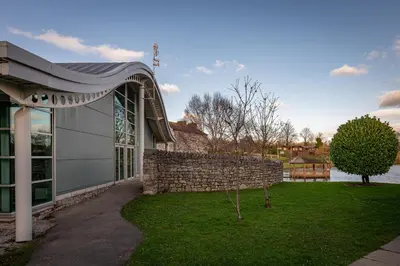 a building with a stone wall next to a yard at Lakeland Lodge in Carnforth
