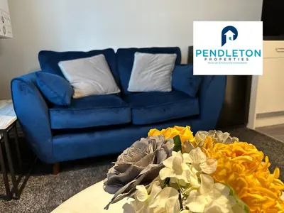 a blue couch in a living room with a table and flowers at Cosy Central APT, 10 Min Walk to UCLAN and Library in Preston