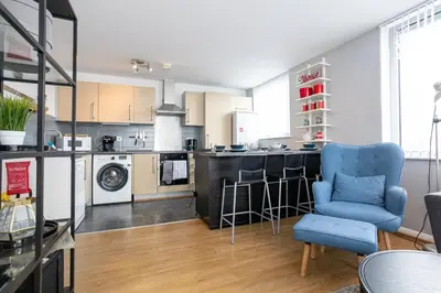 a living room with a blue chair and a kitchen at GuestReady - Modern stay in Bispham House in Liverpool