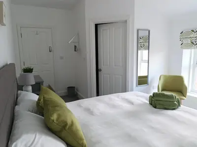 a white bedroom with a bed and a green chair at Victorian Renovation Room 5 in Liverpool