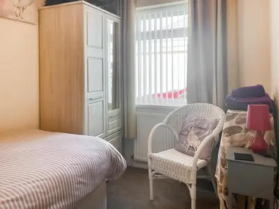 a bedroom with a bed and a chair and a window at The Bay Cottage in Thornton