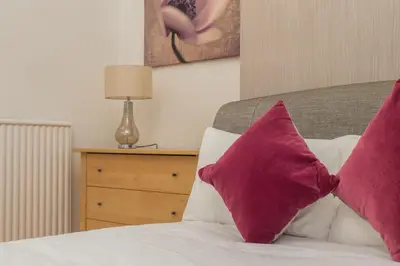 a bed with two purple pillows on it with a night stand at Chestnut Heritage,- Large & Cheerful 5 bedroom house with free parking in Liverpool