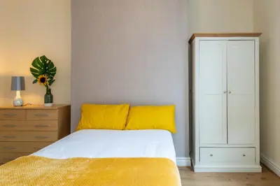 a bedroom with a bed with a yellow blanket and a dresser at Chestnut Heritage,- Large & Cheerful 5 bedroom house with free parking in Liverpool