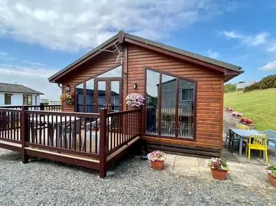 a wooden cabin with a deck and a patio at Lake View Lodge in Millom