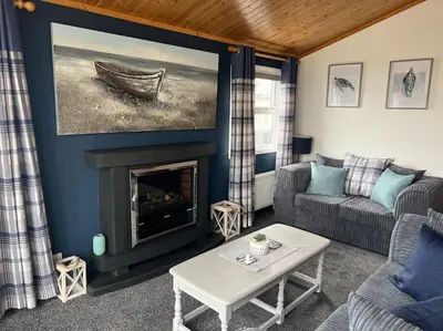 a living room with a fireplace and a painting of a boat at Lake View Lodge in Millom