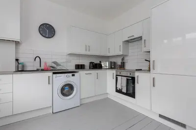 a white kitchen with a washing machine and a clock at Charles Alexander Short Stay - Hove Suite in Lytham St Annes