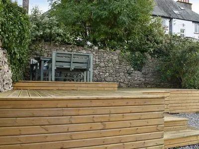 a wooden deck with a chair against a stone wall at Ted's Place in Arnside
