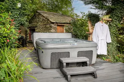 a bath tub sitting on a wooden deck with a robe at Bluebell Wood Cottage - with hot tub in Cartmel