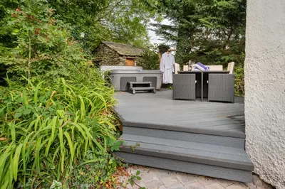a wooden deck with a grill in a garden at Bluebell Wood Cottage - with hot tub in Cartmel