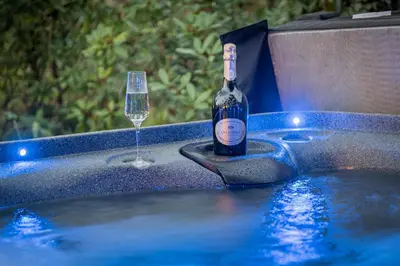 a bottle of wine and a glass in a hot tub at Bluebell Wood Cottage - with hot tub in Cartmel