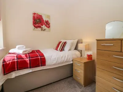 a bedroom with a bed with a red blanket and a dresser at Rolo's Retreat in Grange Over Sands