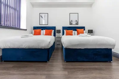 two beds in a room with blue and orange pillows at New Zealand House Apartments by Happy Days in Liverpool
